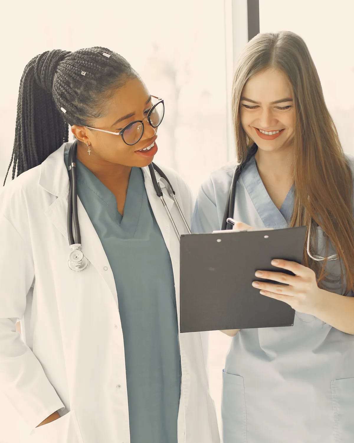 A doctor and a nurse look over notes together by a bright window